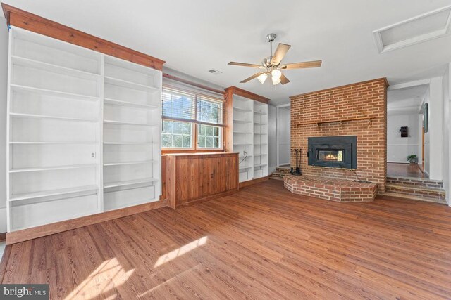 unfurnished living room featuring ceiling fan, built in shelves, a fireplace, and wood-type flooring