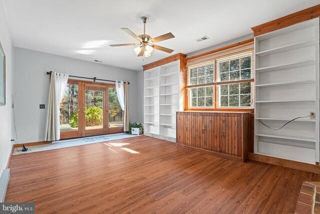 empty room with wood-type flooring, built in features, and ceiling fan