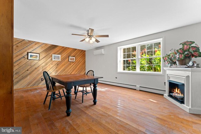 dining space featuring wood walls, a wall mounted AC, baseboard heating, ceiling fan, and light hardwood / wood-style floors