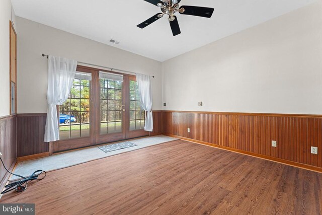 unfurnished room featuring hardwood / wood-style flooring, ceiling fan, and wooden walls