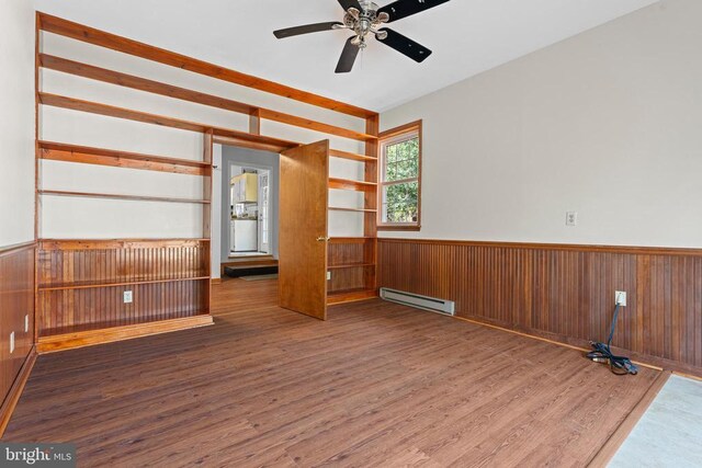 interior space featuring dark hardwood / wood-style flooring, a baseboard heating unit, wooden walls, and ceiling fan