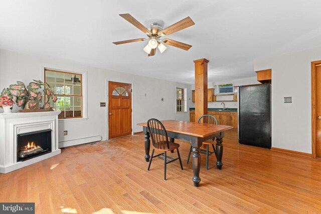 dining area with sink, light hardwood / wood-style flooring, a baseboard radiator, ceiling fan, and decorative columns