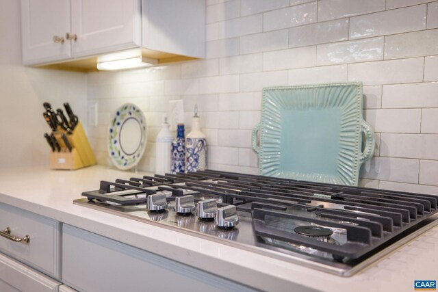 details featuring stainless steel gas cooktop, light countertops, decorative backsplash, and white cabinets