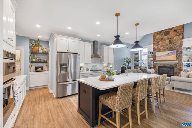 kitchen with white cabinets, wall chimney range hood, appliances with stainless steel finishes, and light countertops