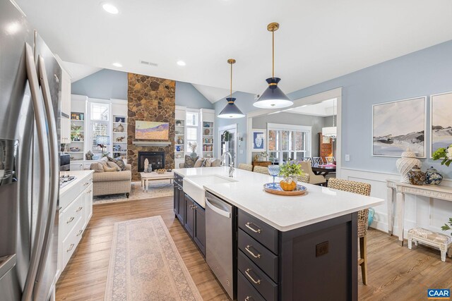 kitchen featuring pendant lighting, light countertops, appliances with stainless steel finishes, open floor plan, and an island with sink