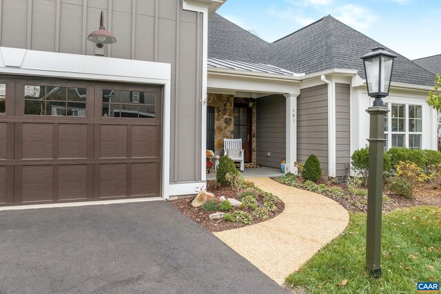 view of exterior entry featuring driveway, a shingled roof, board and batten siding, and an attached garage