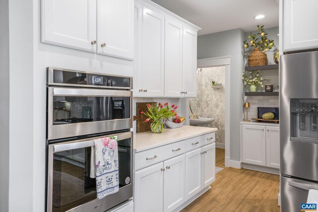 kitchen featuring white cabinets, light countertops, appliances with stainless steel finishes, light wood-type flooring, and decorative backsplash