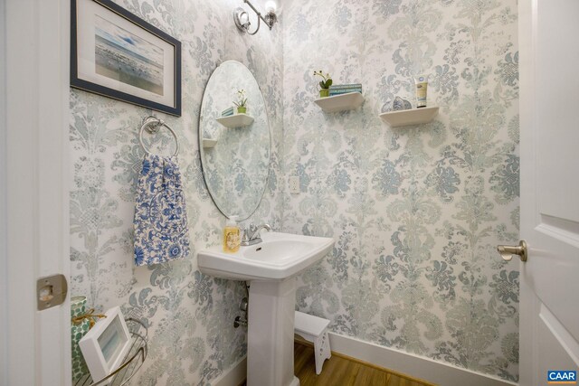 bathroom featuring a sink, baseboards, wood finished floors, and wallpapered walls