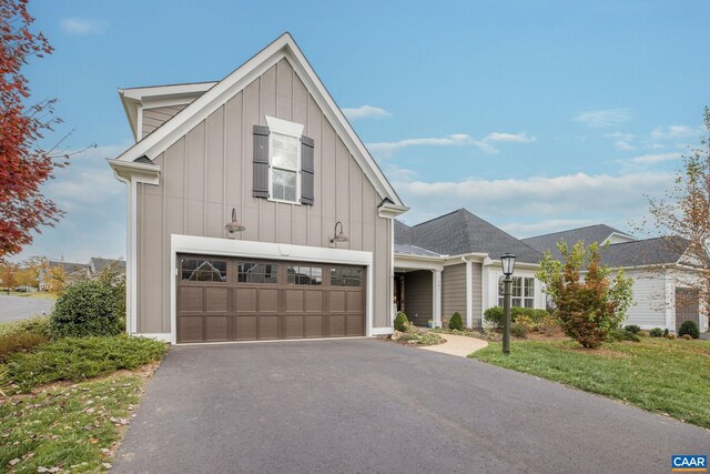 modern farmhouse style home featuring a shingled roof, aphalt driveway, an attached garage, board and batten siding, and a front yard