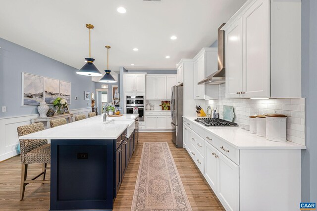 kitchen featuring decorative light fixtures, stainless steel appliances, light countertops, white cabinetry, and a large island with sink