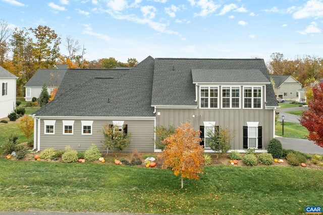 exterior space with board and batten siding, roof with shingles, and a lawn