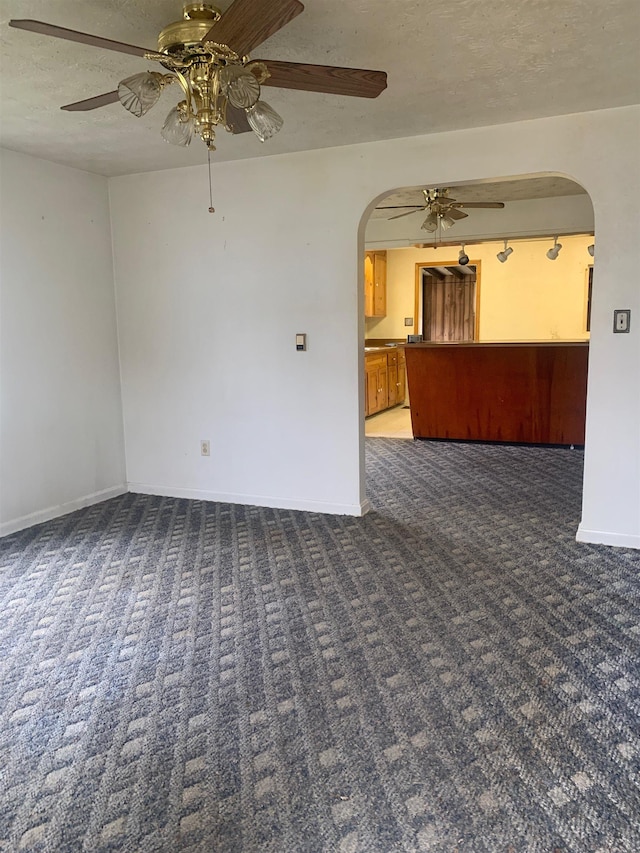 unfurnished room with ceiling fan, dark carpet, and a textured ceiling