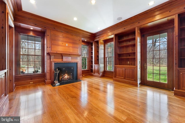 unfurnished living room featuring a healthy amount of sunlight, wood walls, and light hardwood / wood-style flooring