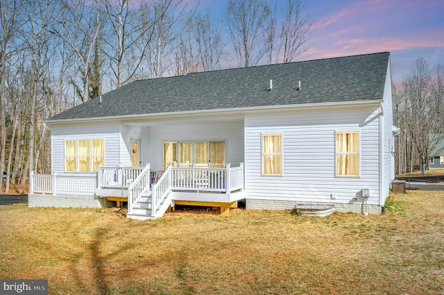 back of property at dusk featuring a shingled roof, a yard, and a deck