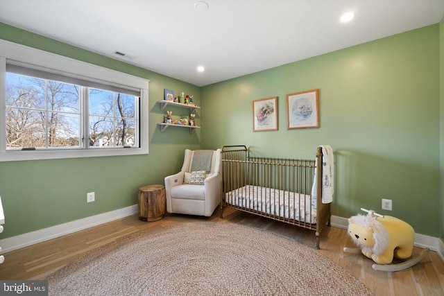 bedroom featuring a nursery area, baseboards, wood finished floors, and recessed lighting