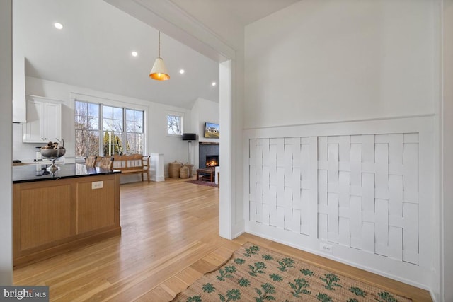 kitchen with decorative light fixtures, light wood finished floors, lofted ceiling, dark countertops, and a lit fireplace