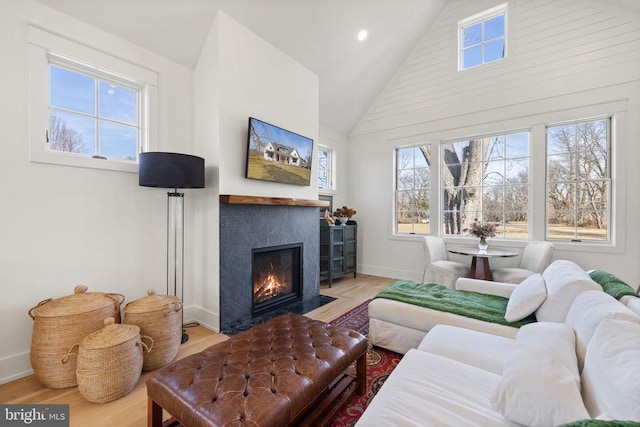 living area with a fireplace with flush hearth, high vaulted ceiling, baseboards, and wood finished floors