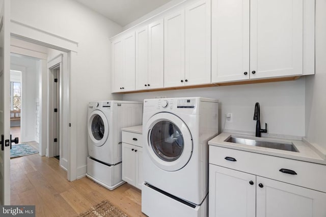 clothes washing area featuring light wood finished floors, separate washer and dryer, a sink, and cabinet space