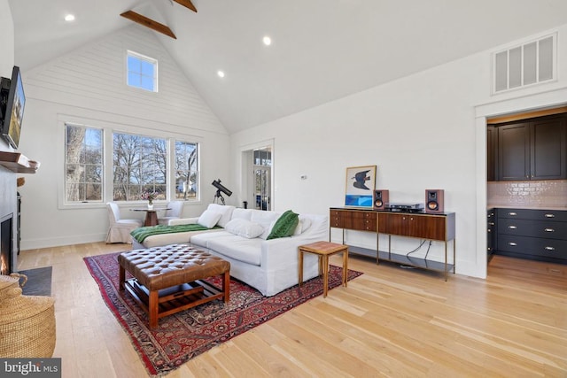 living room with visible vents, a fireplace with flush hearth, light wood-style floors, high vaulted ceiling, and beam ceiling