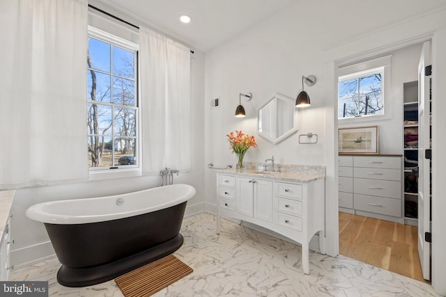 full bath with marble finish floor, plenty of natural light, a freestanding bath, and vanity