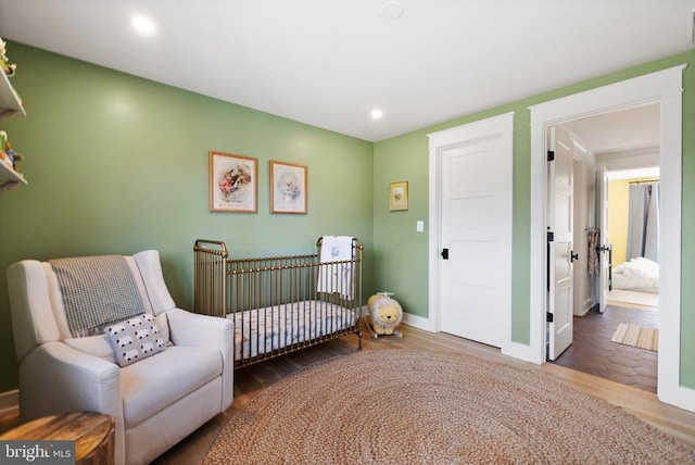 bedroom with baseboards, a crib, wood finished floors, and recessed lighting