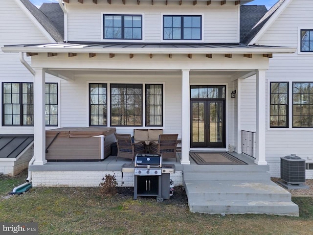 view of exterior entry with a shingled roof, a hot tub, a standing seam roof, central AC, and metal roof