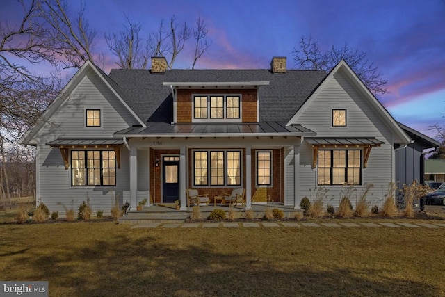 view of front of property featuring metal roof, a porch, a shingled roof, a lawn, and a standing seam roof