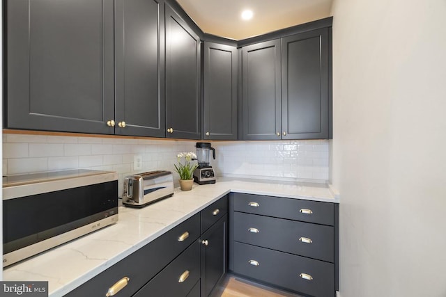 kitchen with light stone countertops, stainless steel microwave, and backsplash