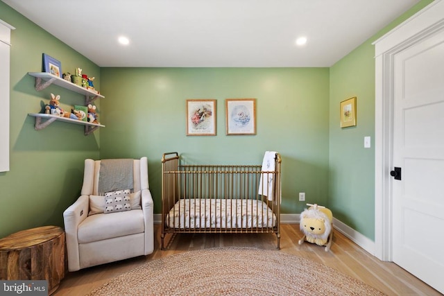 bedroom featuring a crib, recessed lighting, wood finished floors, and baseboards