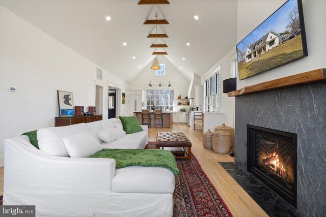 living room featuring recessed lighting, visible vents, a premium fireplace, wood finished floors, and high vaulted ceiling