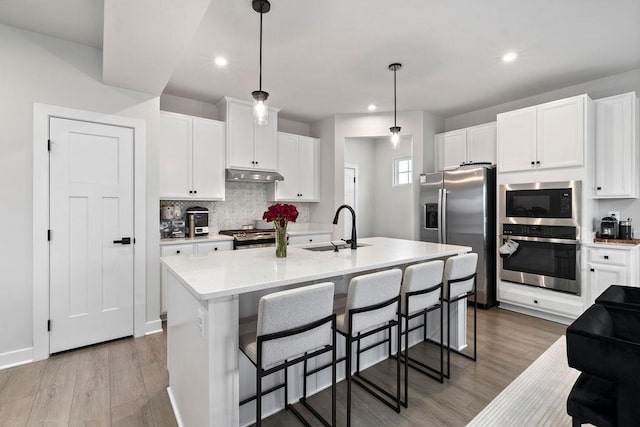 kitchen with under cabinet range hood, wood finished floors, a sink, light countertops, and appliances with stainless steel finishes