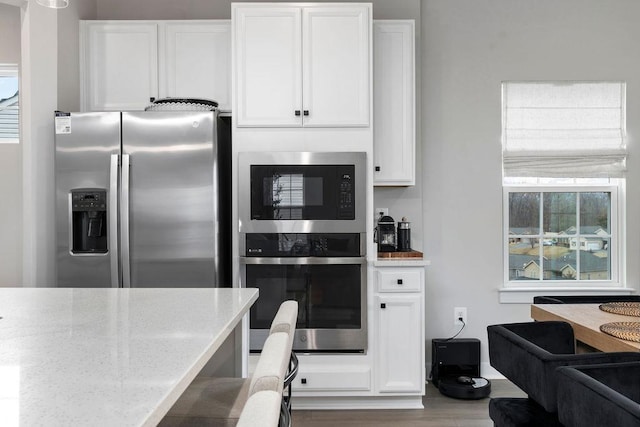 kitchen with stainless steel appliances, light stone counters, wood finished floors, and white cabinetry