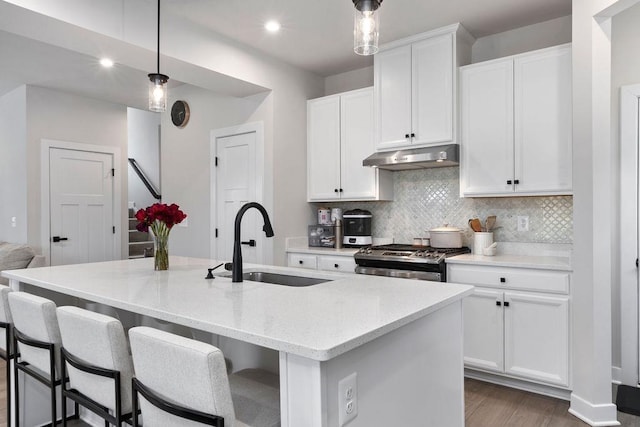 kitchen with decorative backsplash, light stone countertops, under cabinet range hood, stainless steel range with gas cooktop, and a sink