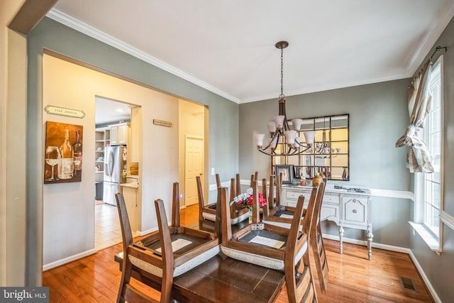 dining space with baseboards, visible vents, wood finished floors, crown molding, and a chandelier