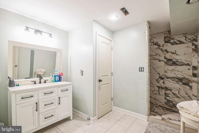 full bathroom with a tile shower, vanity, and baseboards