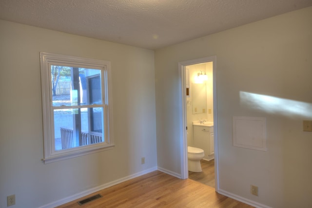 unfurnished bedroom featuring ensuite bathroom, sink, light hardwood / wood-style floors, and a textured ceiling