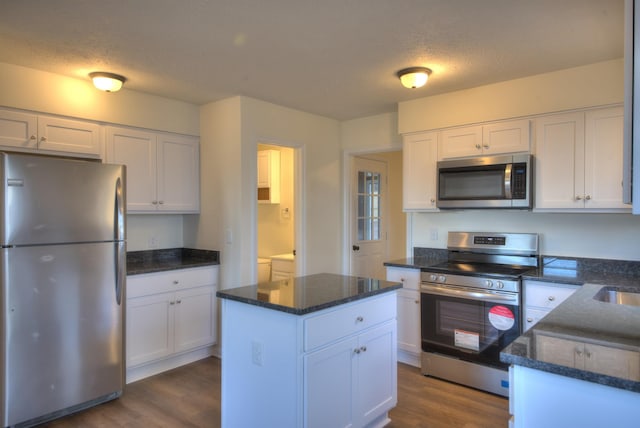 kitchen featuring appliances with stainless steel finishes, white cabinetry, dark hardwood / wood-style flooring, dark stone counters, and a textured ceiling