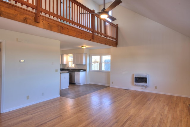 unfurnished living room with ceiling fan, a towering ceiling, heating unit, and light wood-type flooring