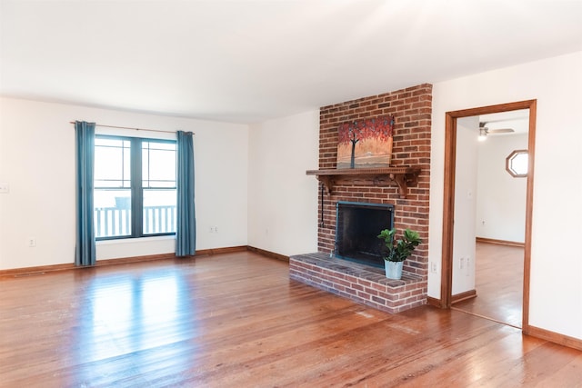 unfurnished living room with a brick fireplace, wood finished floors, and baseboards