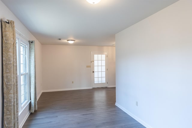 unfurnished room featuring dark wood-type flooring, visible vents, and baseboards