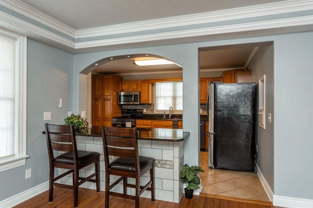 kitchen with sink, ornamental molding, appliances with stainless steel finishes, a kitchen breakfast bar, and decorative backsplash