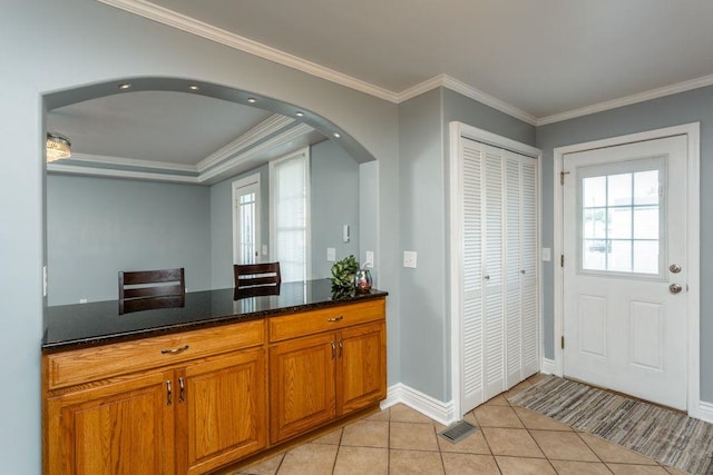 kitchen with light tile patterned floors, ornamental molding, and dark stone counters