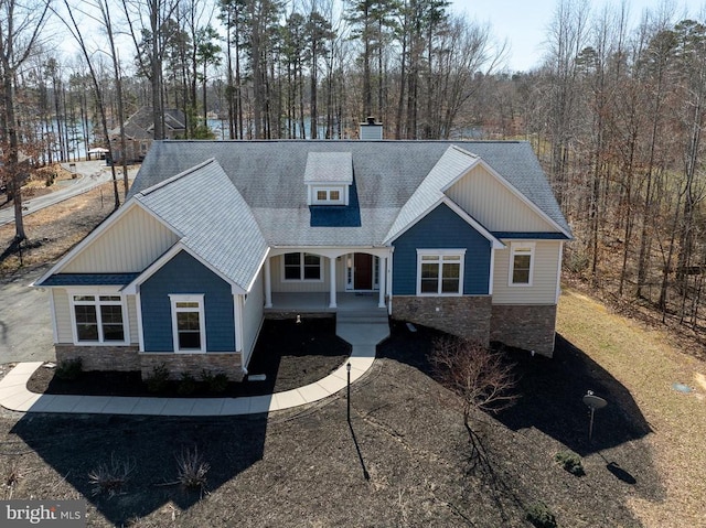 craftsman-style house with a shingled roof, a porch, stone siding, and a chimney