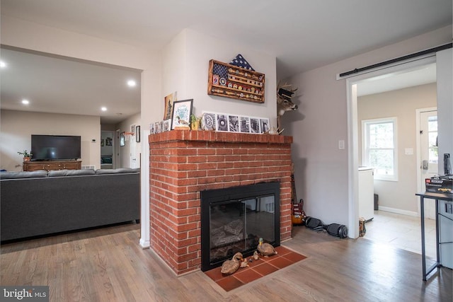 living area with a brick fireplace, a barn door, wood finished floors, and recessed lighting