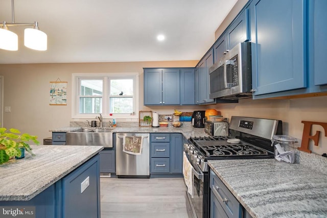 kitchen featuring stainless steel appliances, light wood-type flooring, blue cabinetry, pendant lighting, and a sink