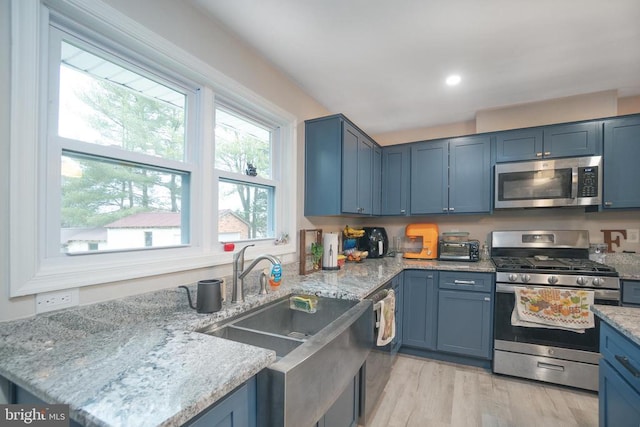 kitchen with appliances with stainless steel finishes, blue cabinets, a sink, and light wood-style flooring