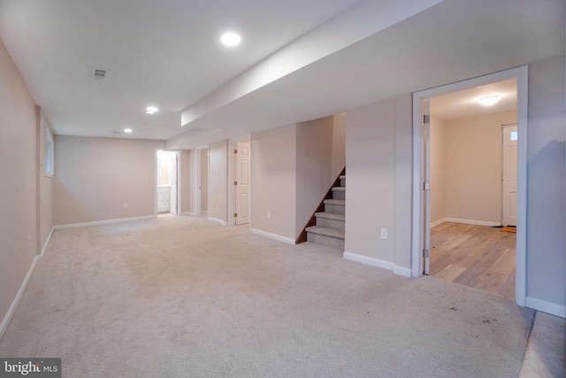 finished basement with stairs, baseboards, visible vents, and light colored carpet