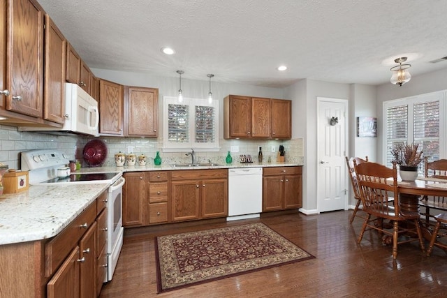 kitchen with a sink, dark wood finished floors, brown cabinets, and white appliances