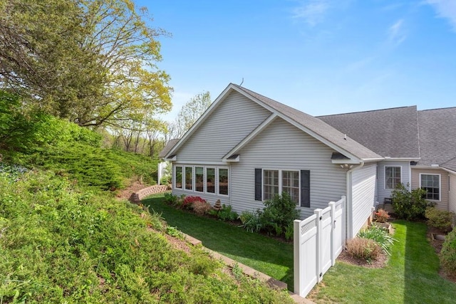 view of home's exterior featuring a shingled roof, fence, and a yard