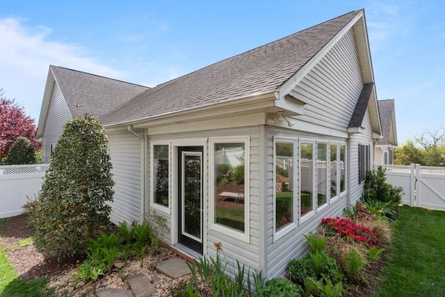 view of home's exterior with roof with shingles, fence, and a gate